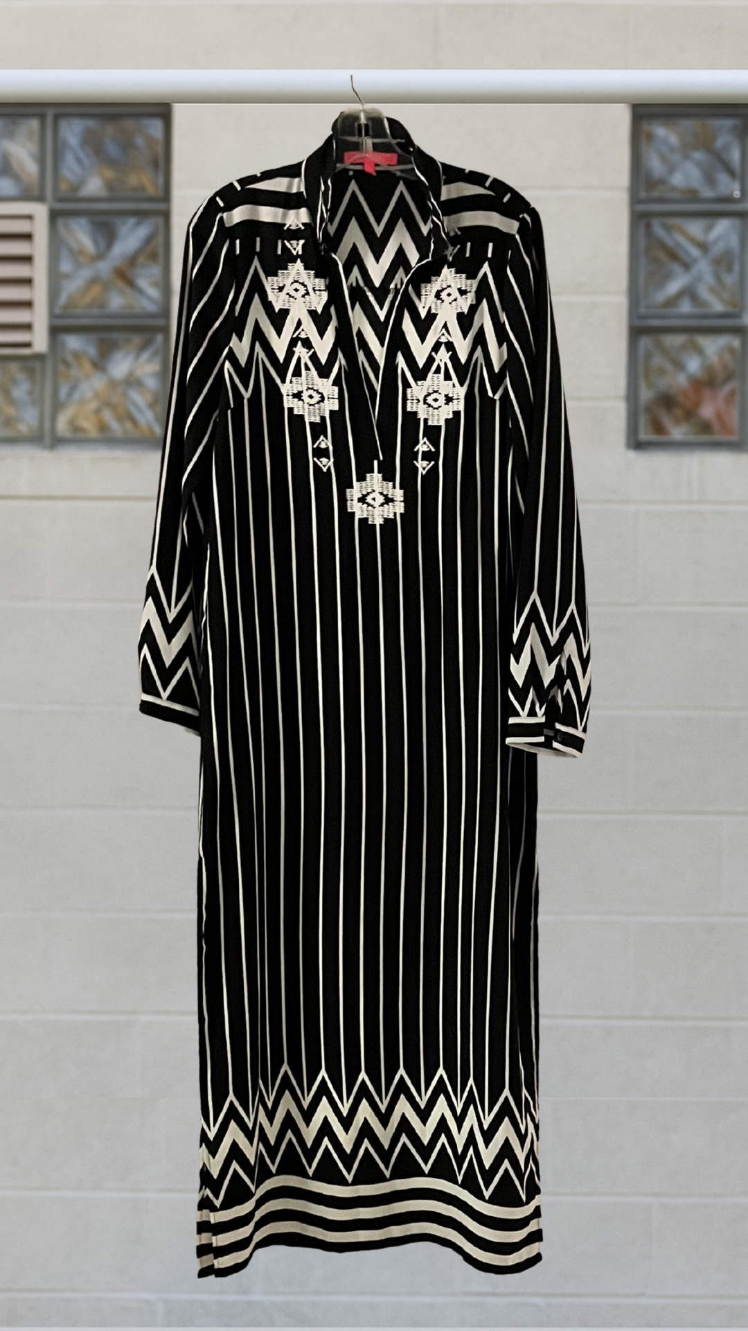 Black dress with white patterns on a hanger against a tiled wall.