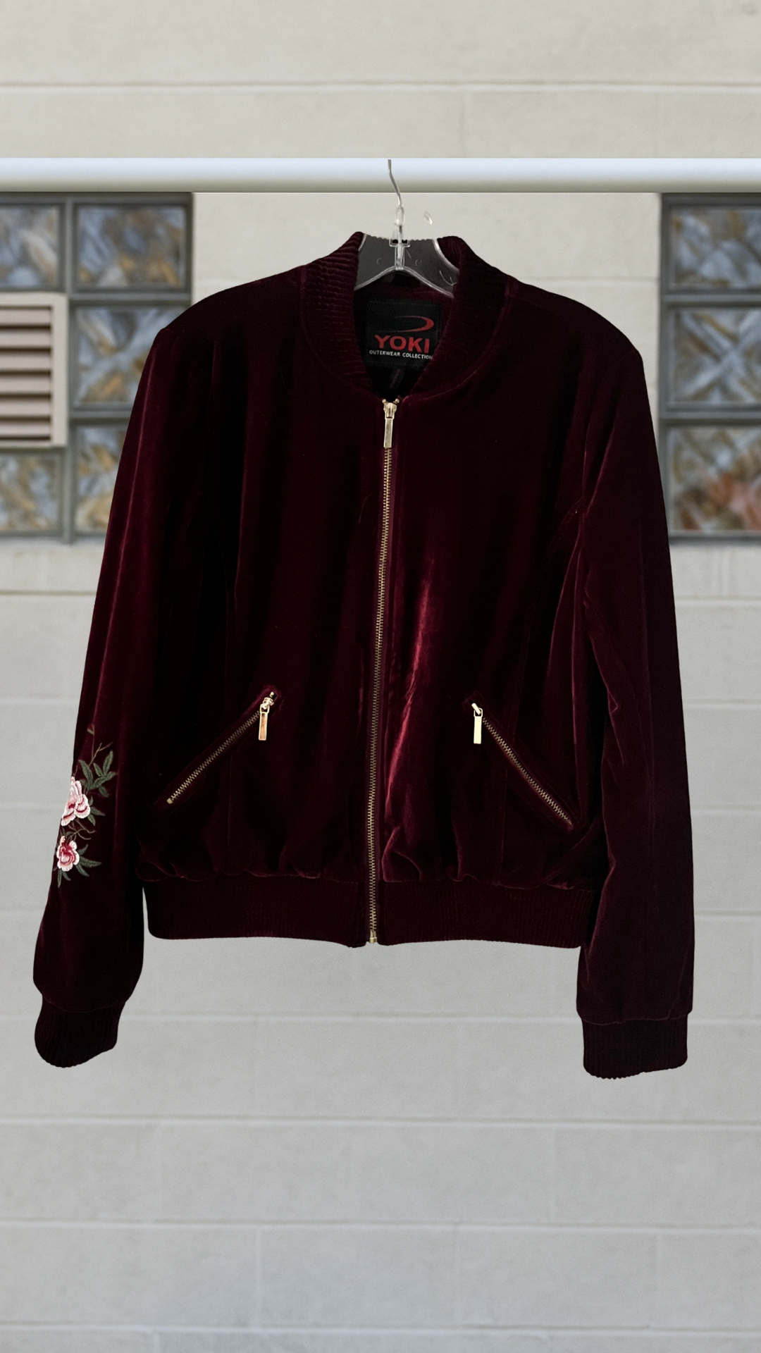 a velvet jacket with gold zippers on a hanger against a white wall