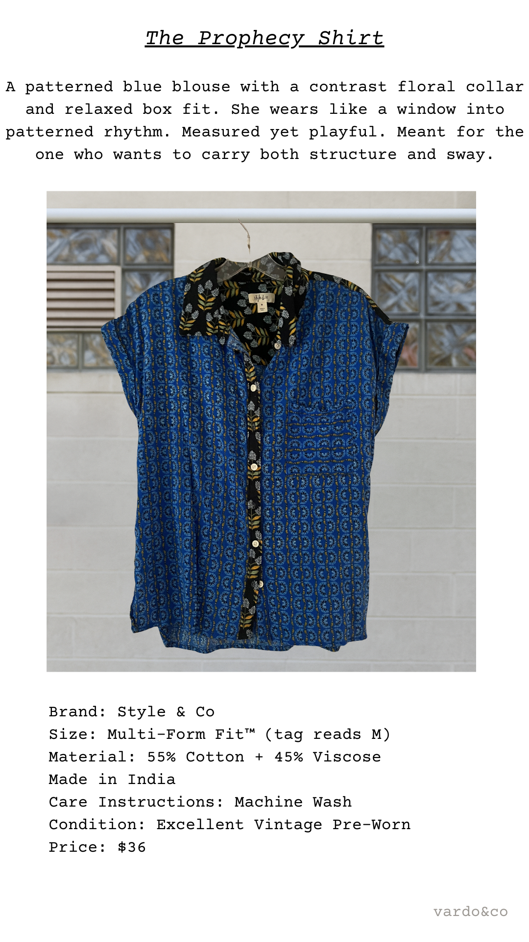 Blue patterned blouse with floral collar on a hanger against a tiled wall.