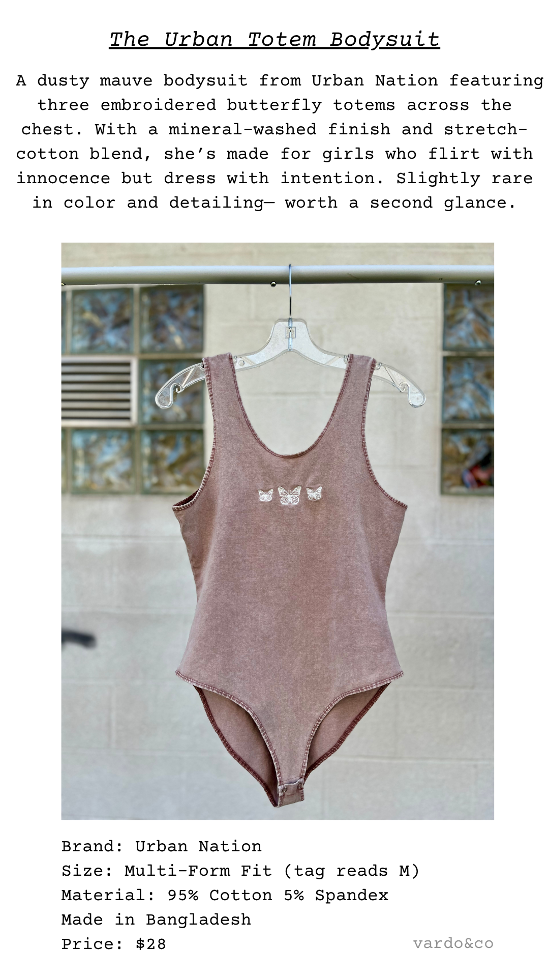 Dusty mauve mineral-washed bodysuit hanging on a clear hanger, displayed against a light brick wall. The bodysuit features three white embroidered butterflies across the chest and a snap-closure bottom.