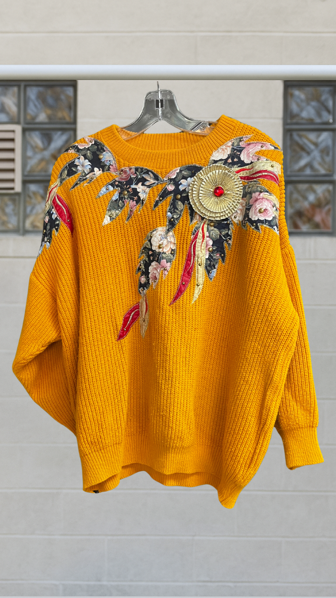 a yellow sweater with floral embellishments on hanger against a white background