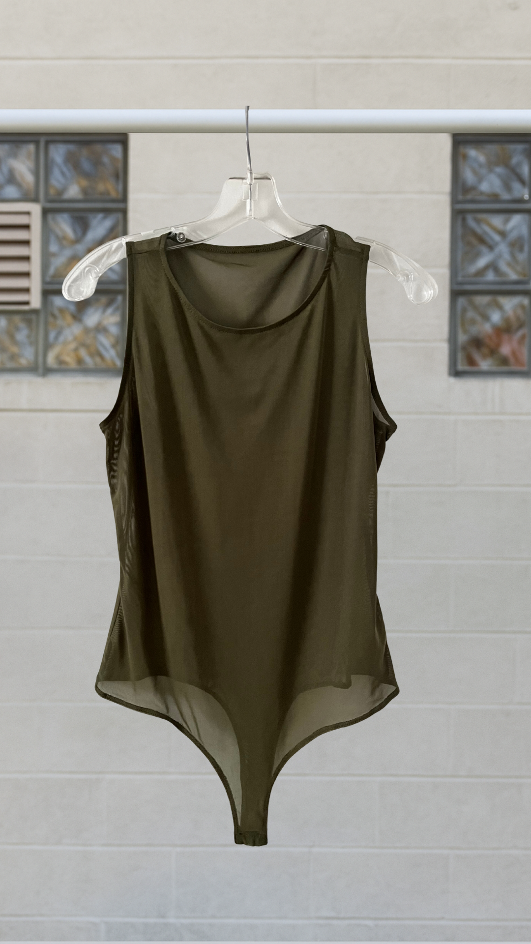 a sheer green bodysuit on a hanger against a white background