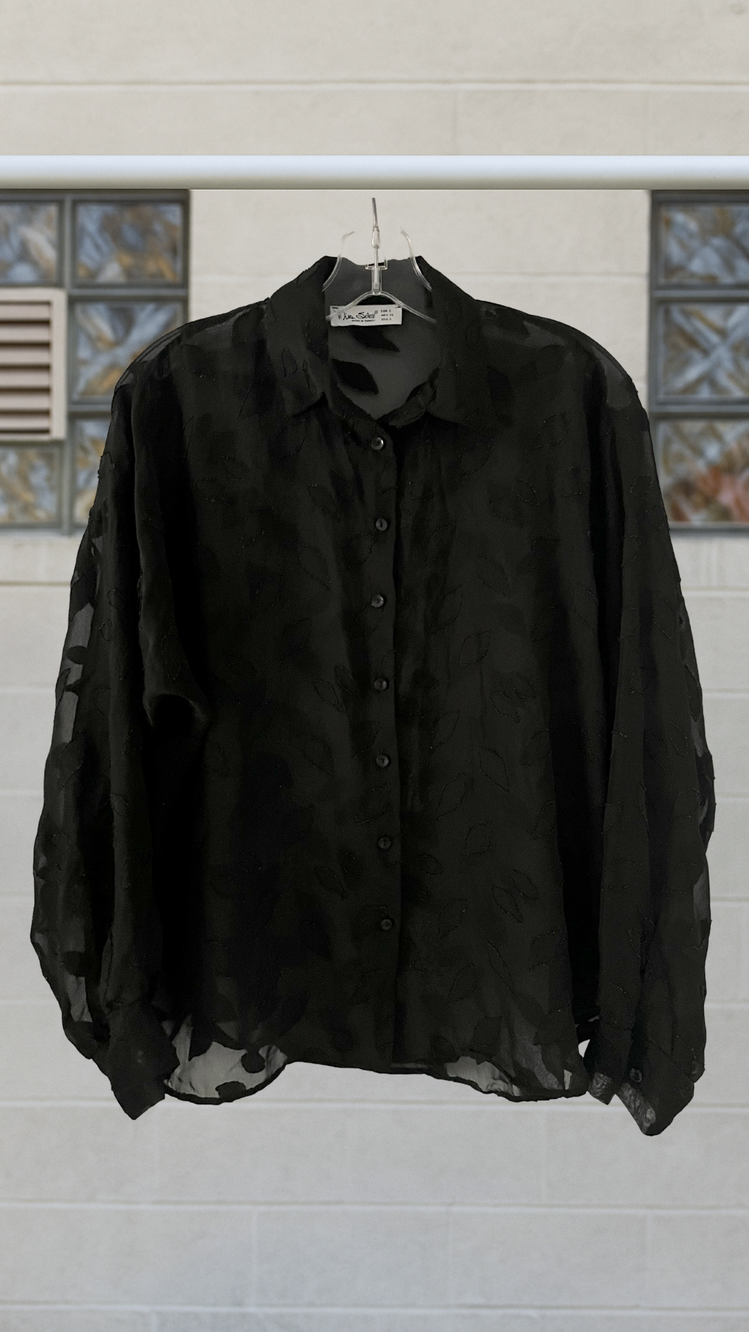 a sheer black button down shirt on a hanger against a neutral background
