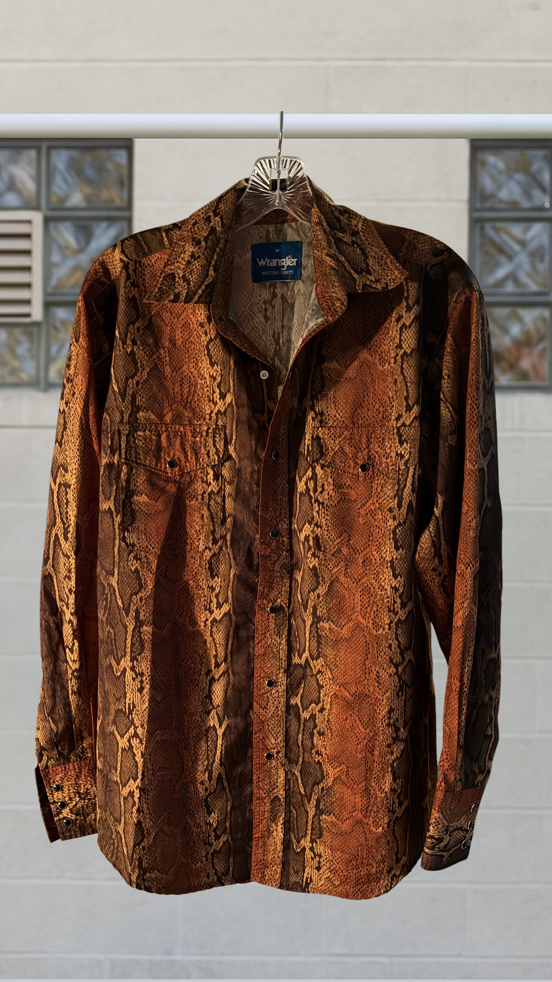 a button down shirt with snake skin patterning on a hanger against a white background