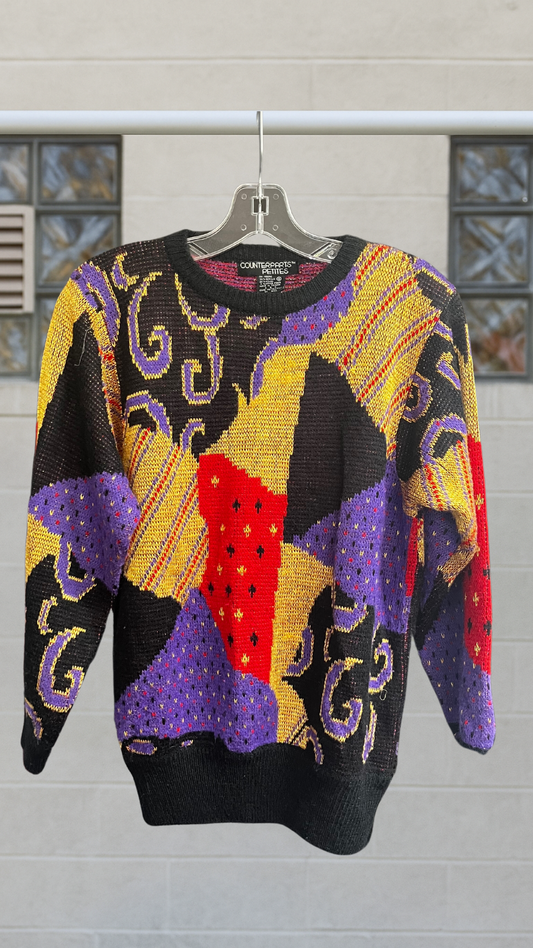 Colorful vintage abstract sweater with bold patchwork print in red, yellow, purple, and black, hanging on a clear hanger.