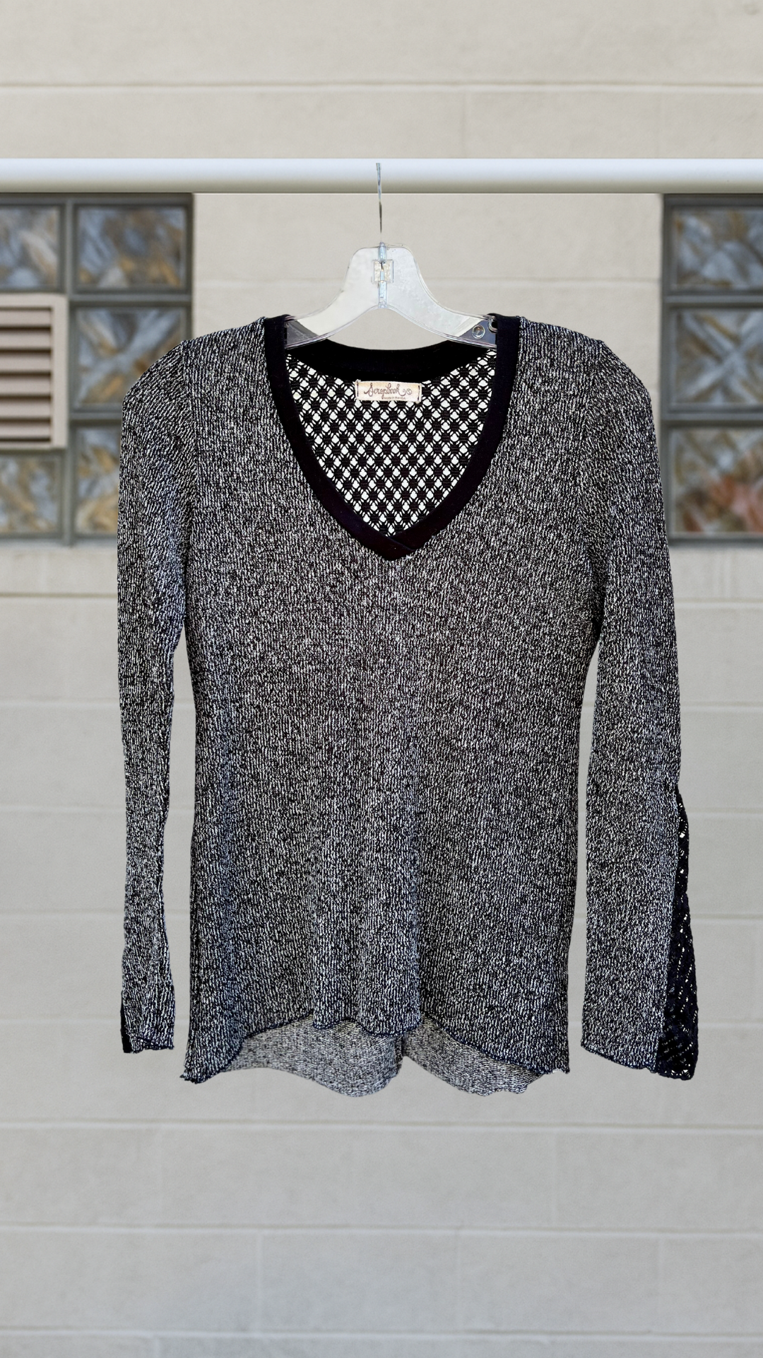 Black and white textured knit shirt with diamond lace back and bell sleeves, hanging on hanger outdoors