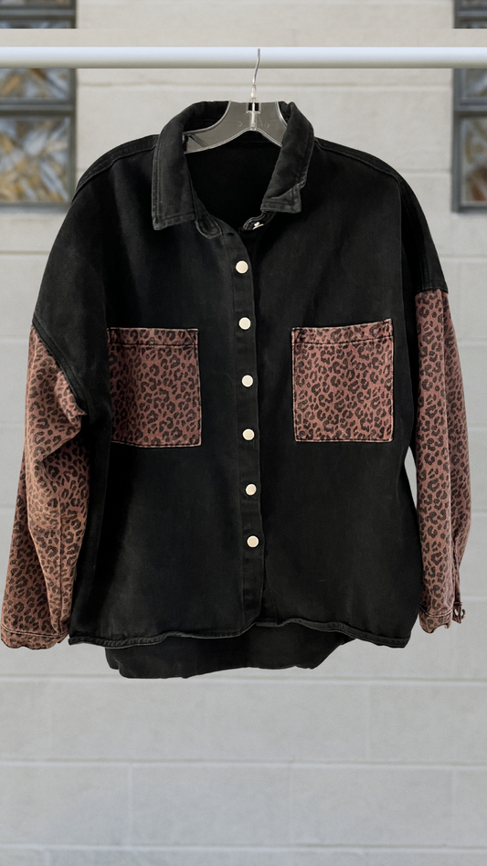 Black denim overshirt with cheetah-print pockets and sleeves, button-front closure, and oversized fit, displayed on hanger.

