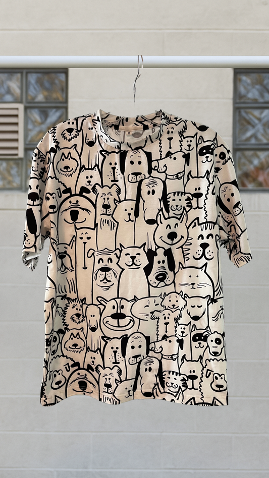 Cream graphic tee with all-over cartoon cat and dog print in black ink. Short sleeves and crew neck.
