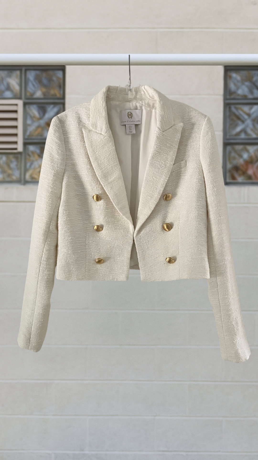 White blazer with gold buttons on a hanger against a light background