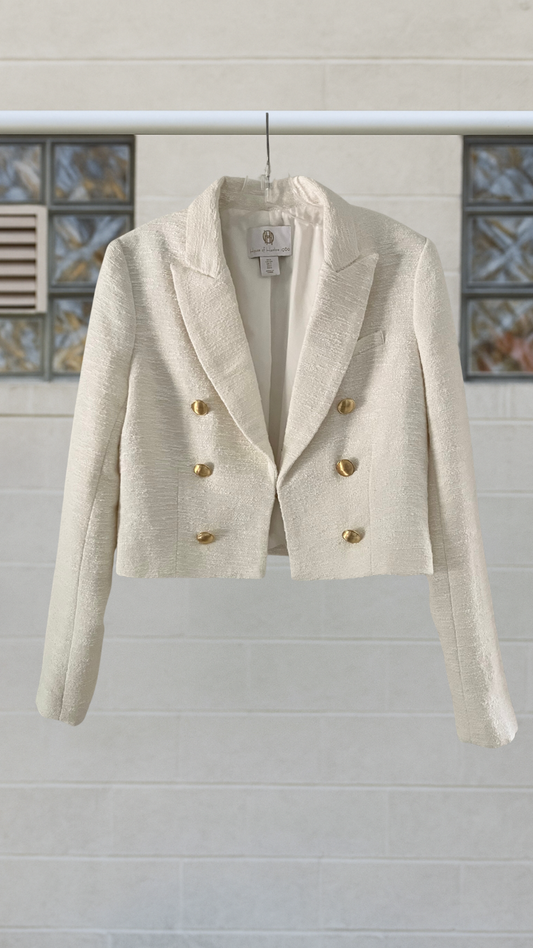 White blazer with gold buttons on a hanger against a light background