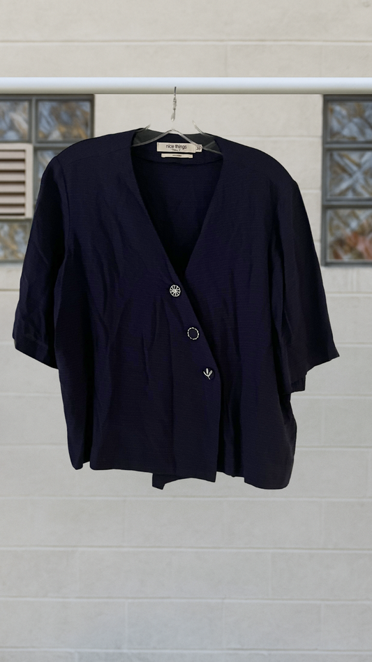 Navy blue shirt on a hanger against a light gray wall.