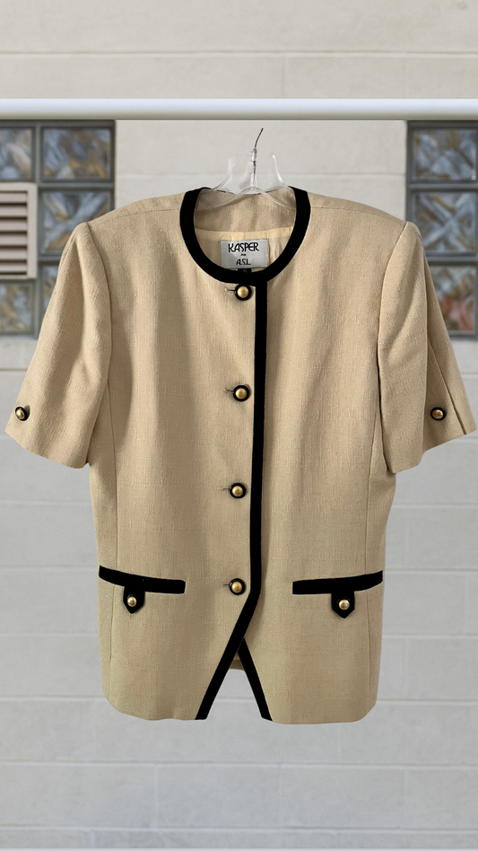 Beige jacket with black accents on a hanger against a light gray wall.