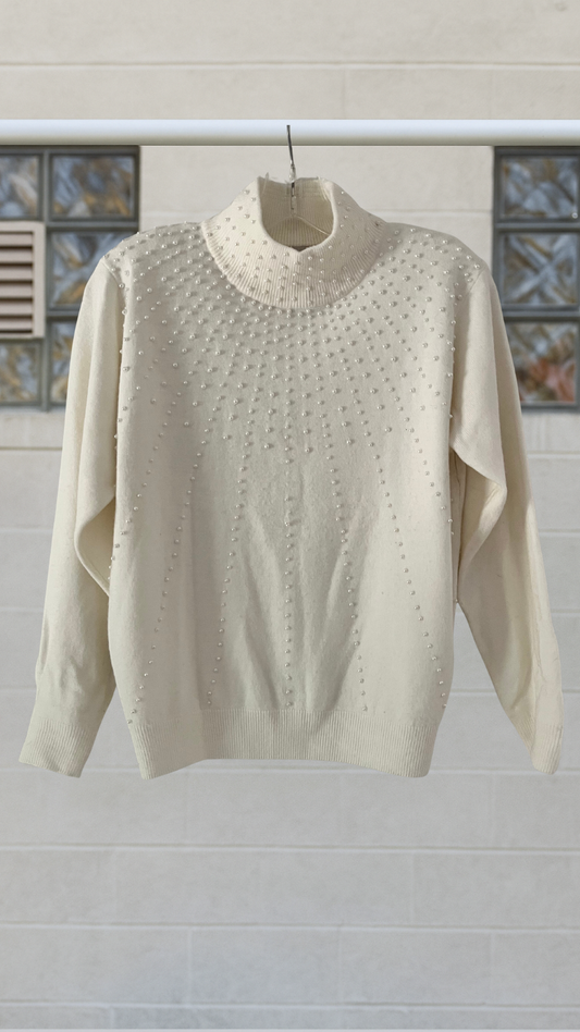 A cream knit sweater with pearls scattered across the front in a radiant constellation design
