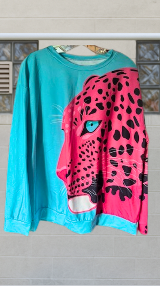 Oversized sweatshirt with a bold pink leopard face on a turquoise background, hanging against a tiled wall.