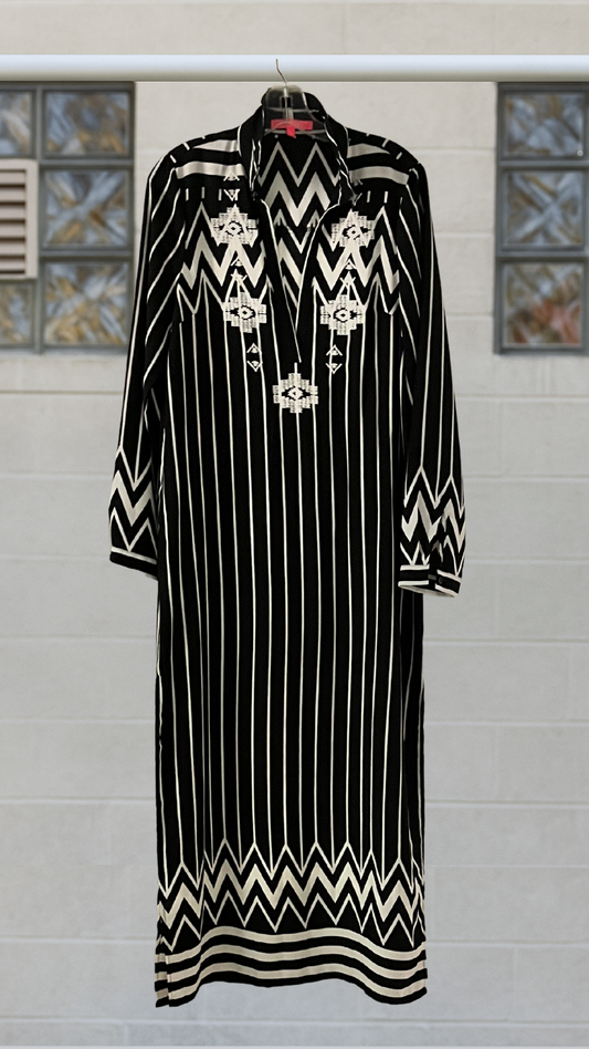 Black dress with white patterns on a hanger against a tiled wall.