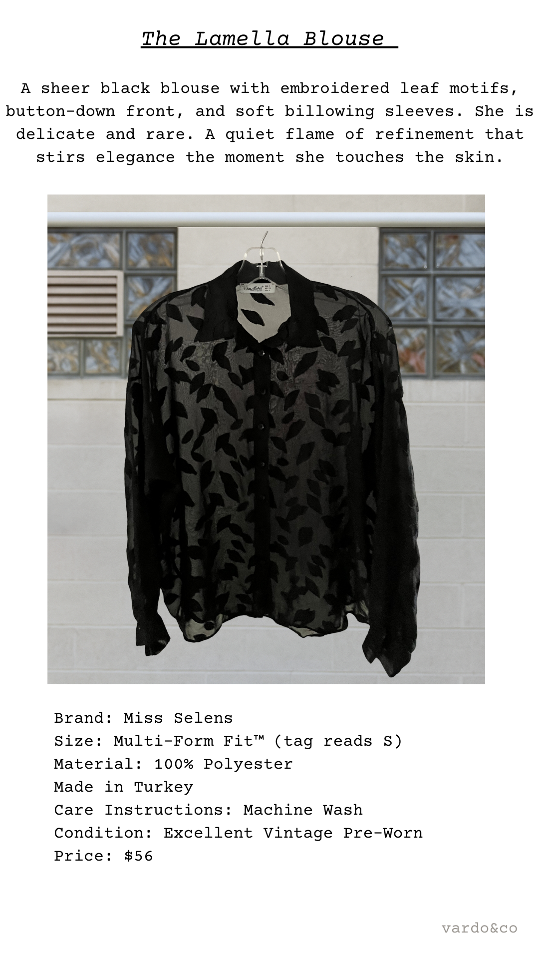 Black sheer blouse with embroidered leaf motifs on a hanger against a tiled wall.