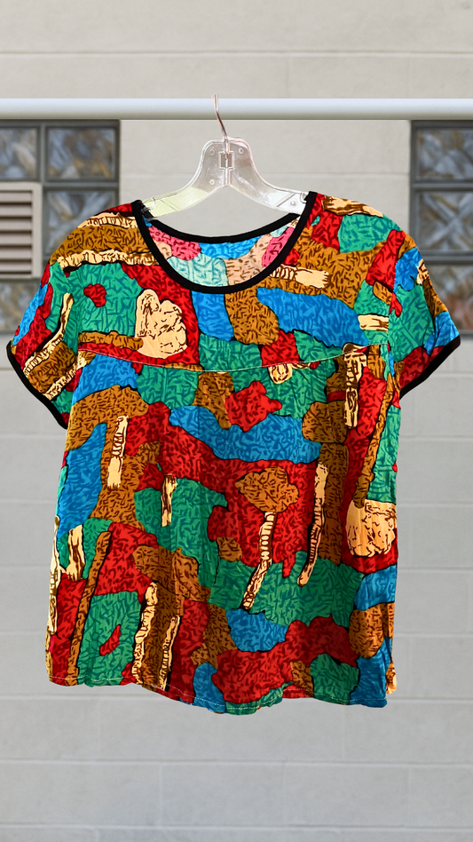Colorful abstract printed short sleeve blouse with black trim, hanging on clear hanger.