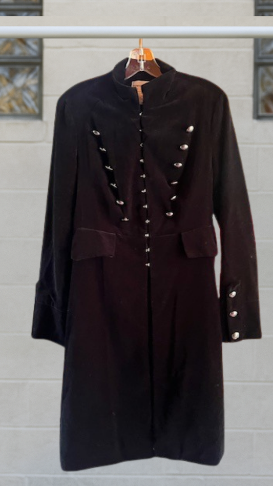 Long black duster-style jacket with silver buttons and mock neck, hanging on a clear hanger against a brick wall.