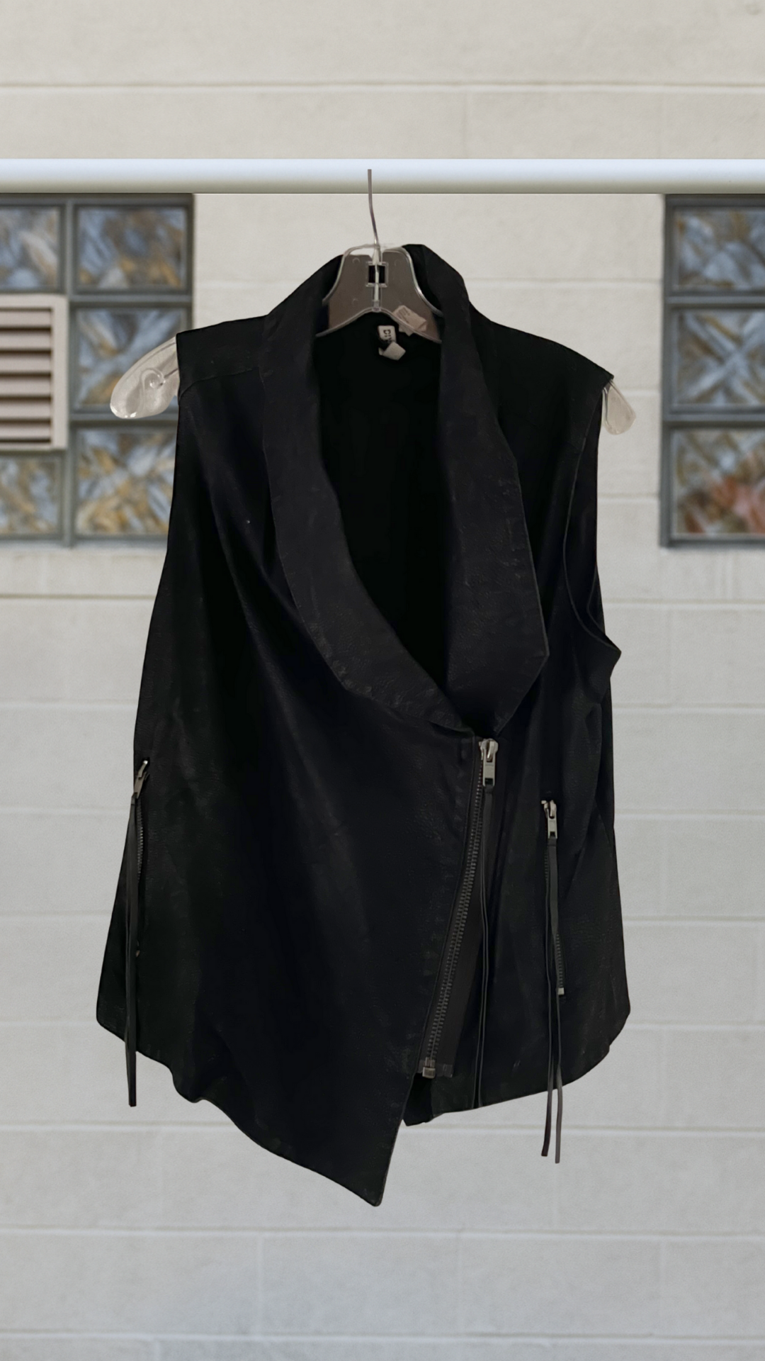black faux leather assymetrical vest on a hanger with a white background