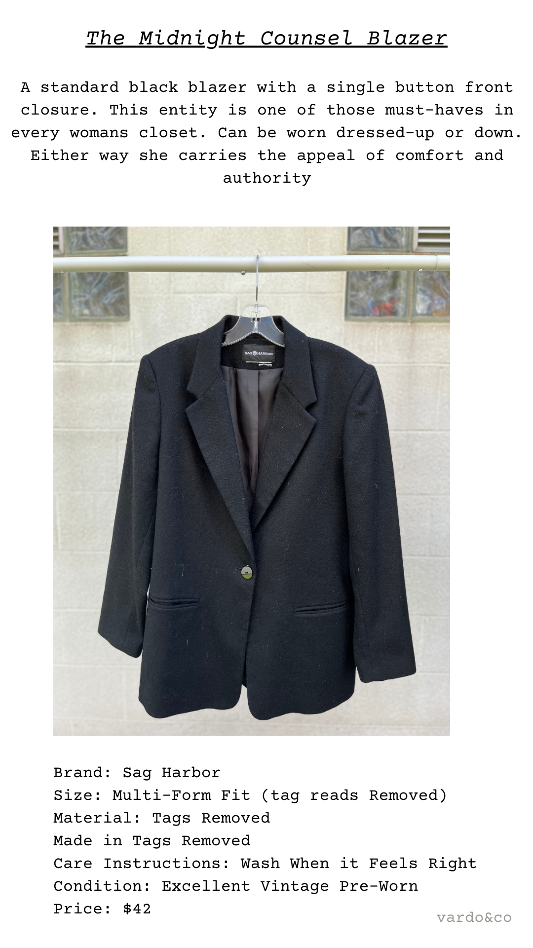 The Midnight Counsel Blazer shown front-facing on hanger, clean lines and classic tailoring displayed against light brick backdrop.
