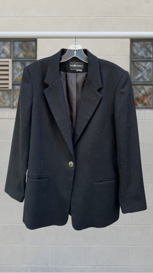 Black single-button blazer with notched lapel and welt pockets, timeless Sag Harbor design photographed front-on against neutral wall.
