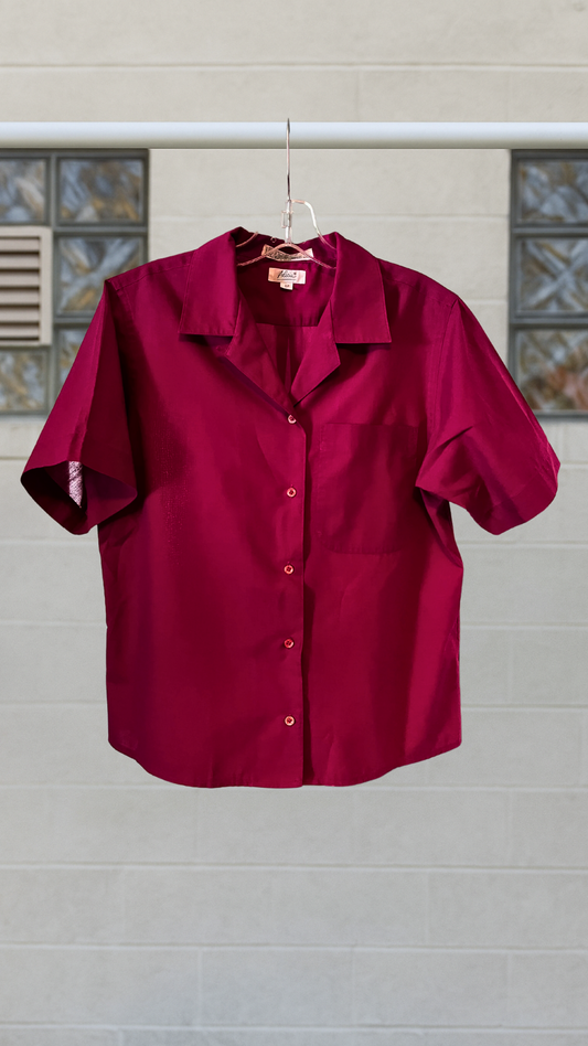 Solid magenta short sleeve button-up shirt with a front pocket and notched collar, hanging on a hanger outdoors.