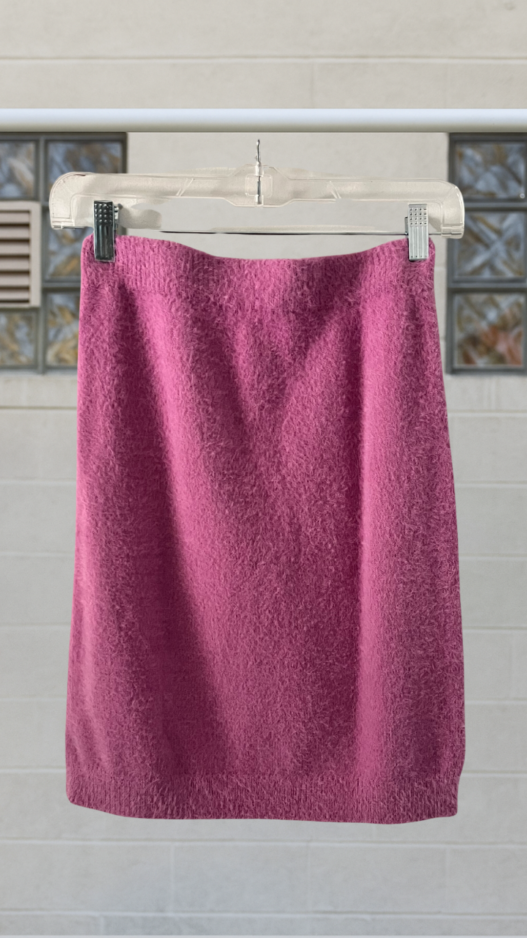 Magenta angora-textured bodycon skirt hanging on clear hanger in front of a tiled wall
