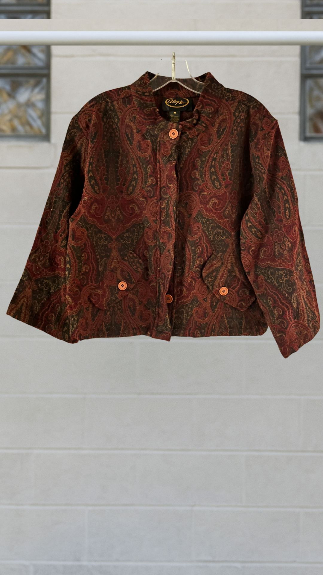The Ornate Tapestry Jacket in deep rust paisley weave with mandarin collar and cropped fit, featuring wide sleeves and buttoned front flap pockets.
