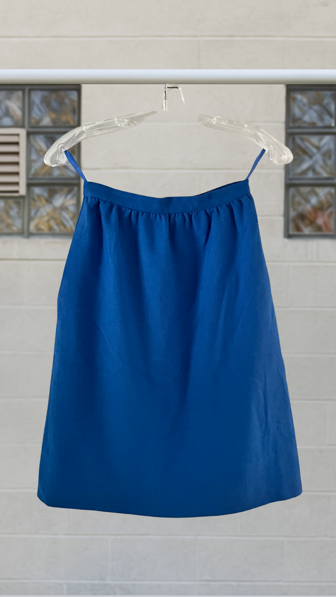 Blue skirt on a hanger against a light-colored wall with decorative elements.