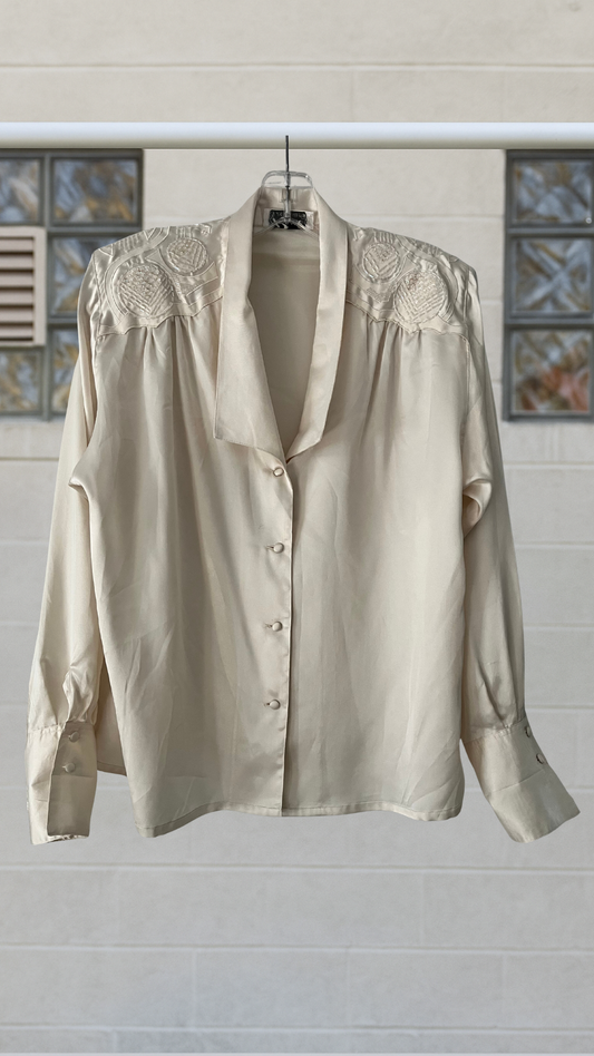 Silky ivory blouse with beaded shoulders, padded structure, and covered buttons
