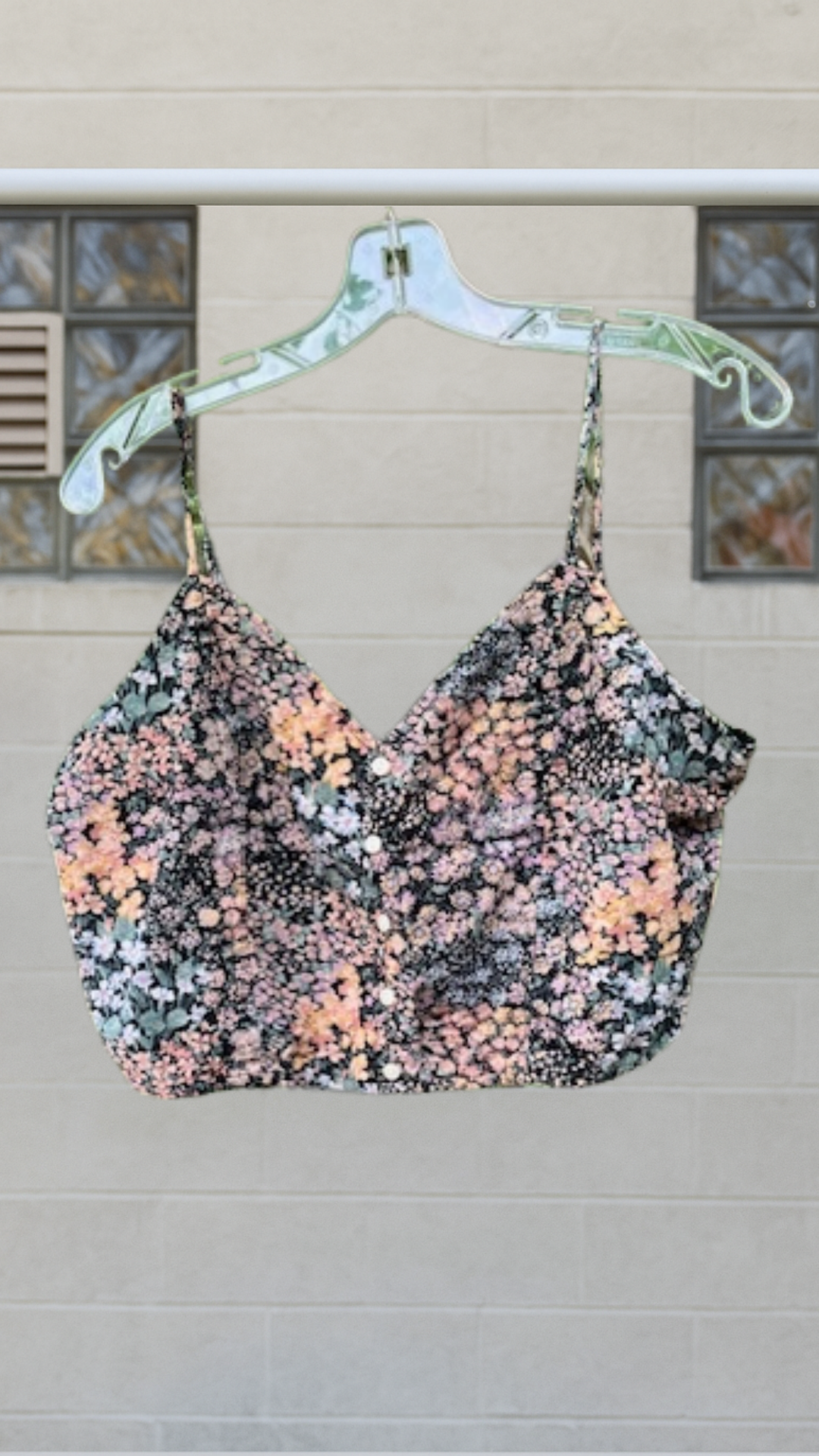 Floral cropped blouse with spaghetti straps and button-up front, hanging on clear hanger against neutral background
