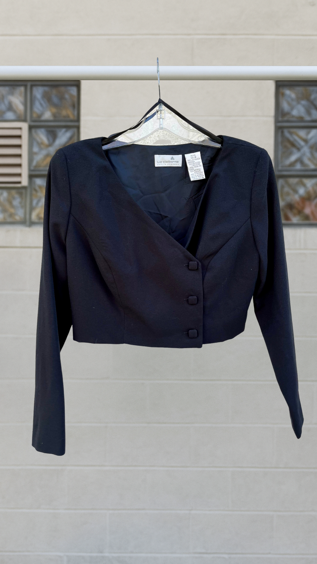 Cropped asymmetrical black blazer with fabric-covered buttons and shoulder pads.