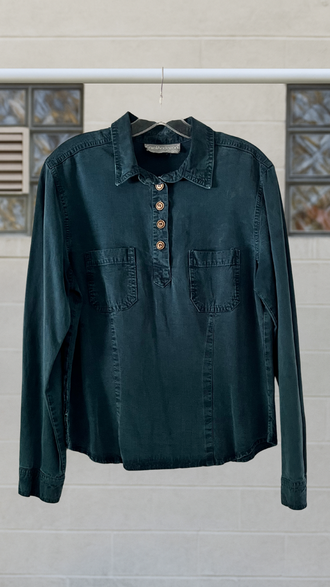 Dark green shirt with button details on a hanger against a neutral background