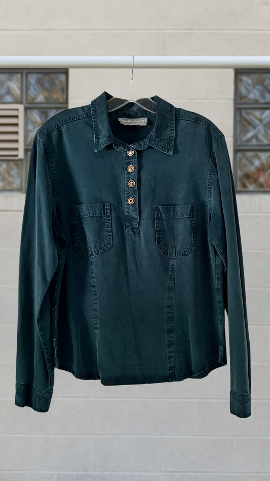 Dark green shirt with button details on a hanger against a neutral background