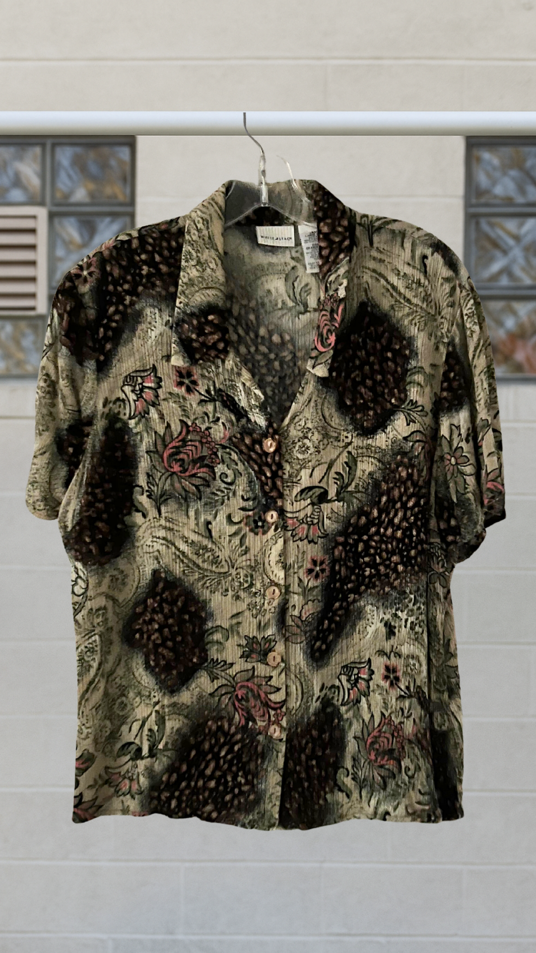 Button down shirt with floral patterns on a hanger against a neutral background