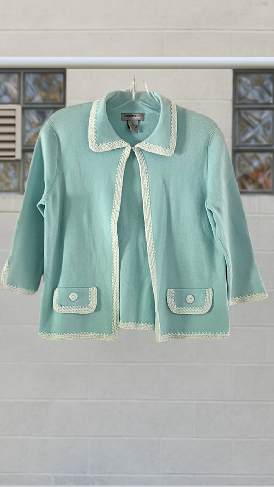 Light blue cardigan with white trim hanging on a rack against a neutral background