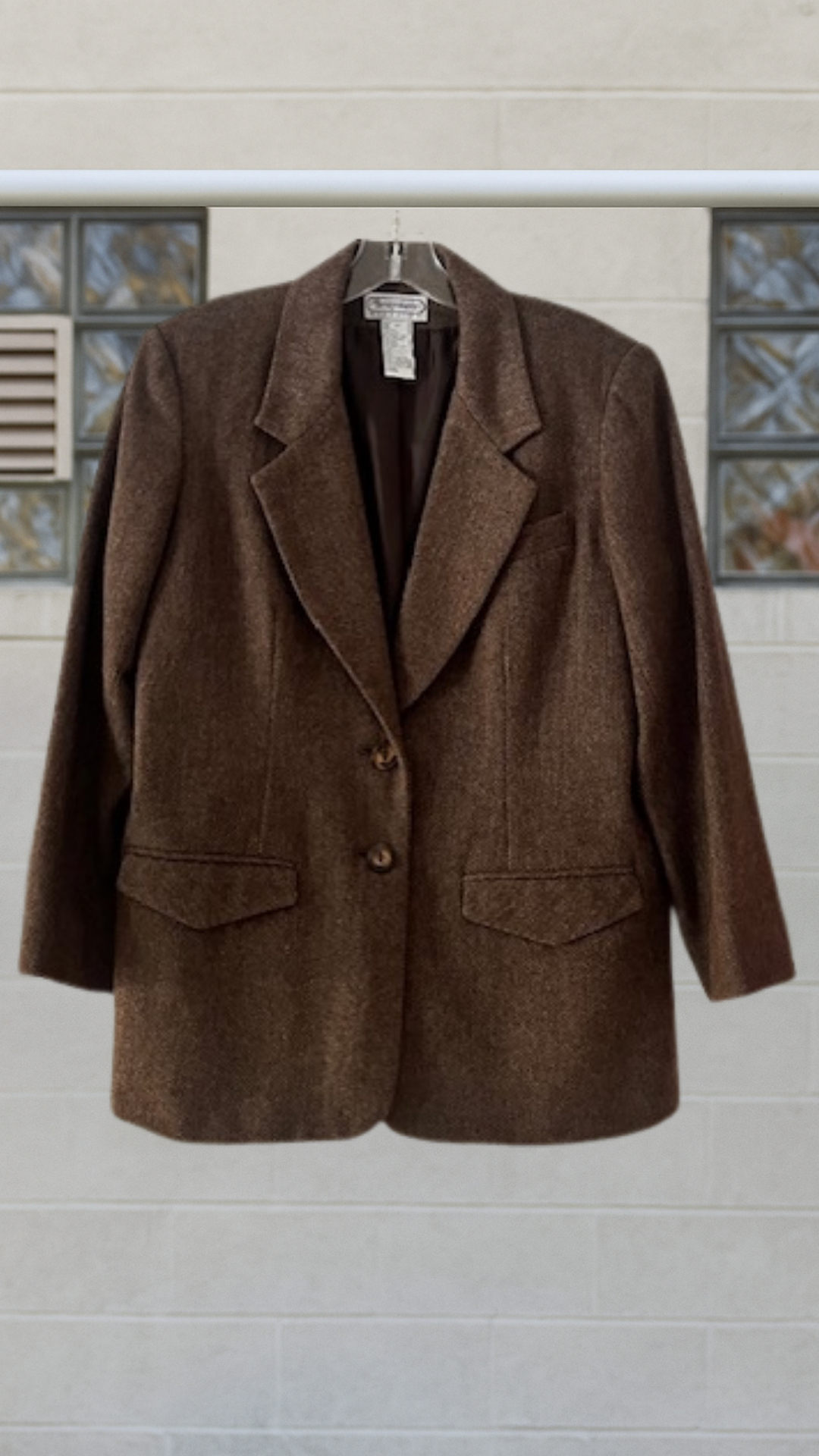 Brown blazer on a hanger against a light-colored wall with decorative tiles.