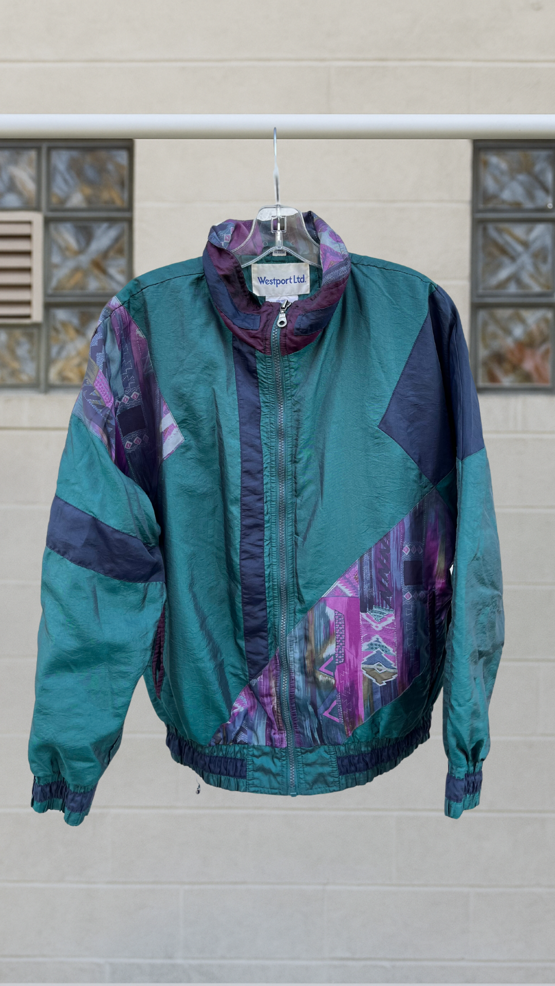 Teal and purple vintage windbreaker jacket with abstract patchwork patterns and a zip front, shown hanging outdoors.