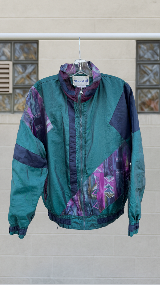 Teal and purple vintage windbreaker jacket with abstract patchwork patterns and a zip front, shown hanging outdoors.