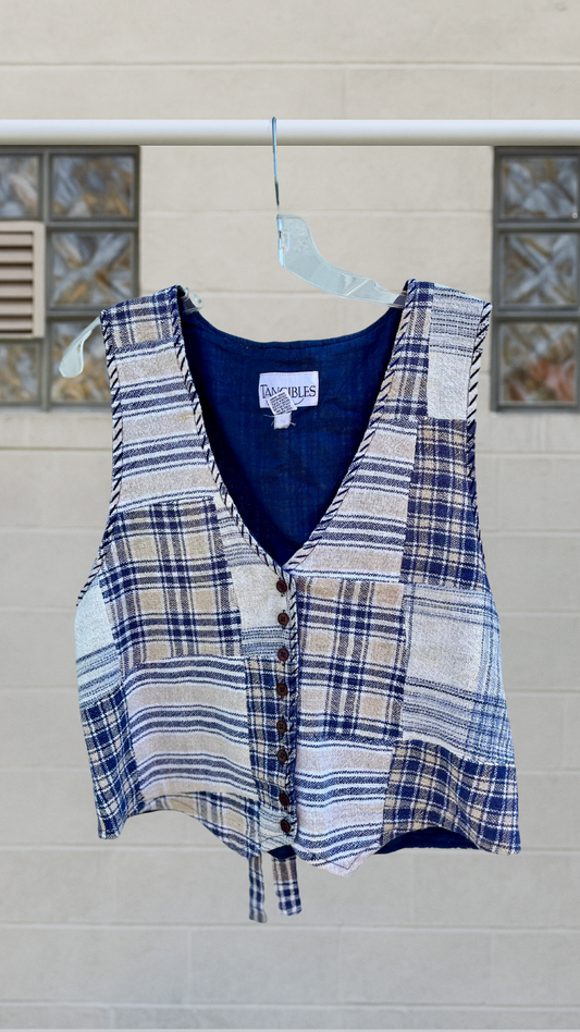 Vintage patchwork vest in navy and sand tones, with rear tie and full button front, hanging on a clear hanger.