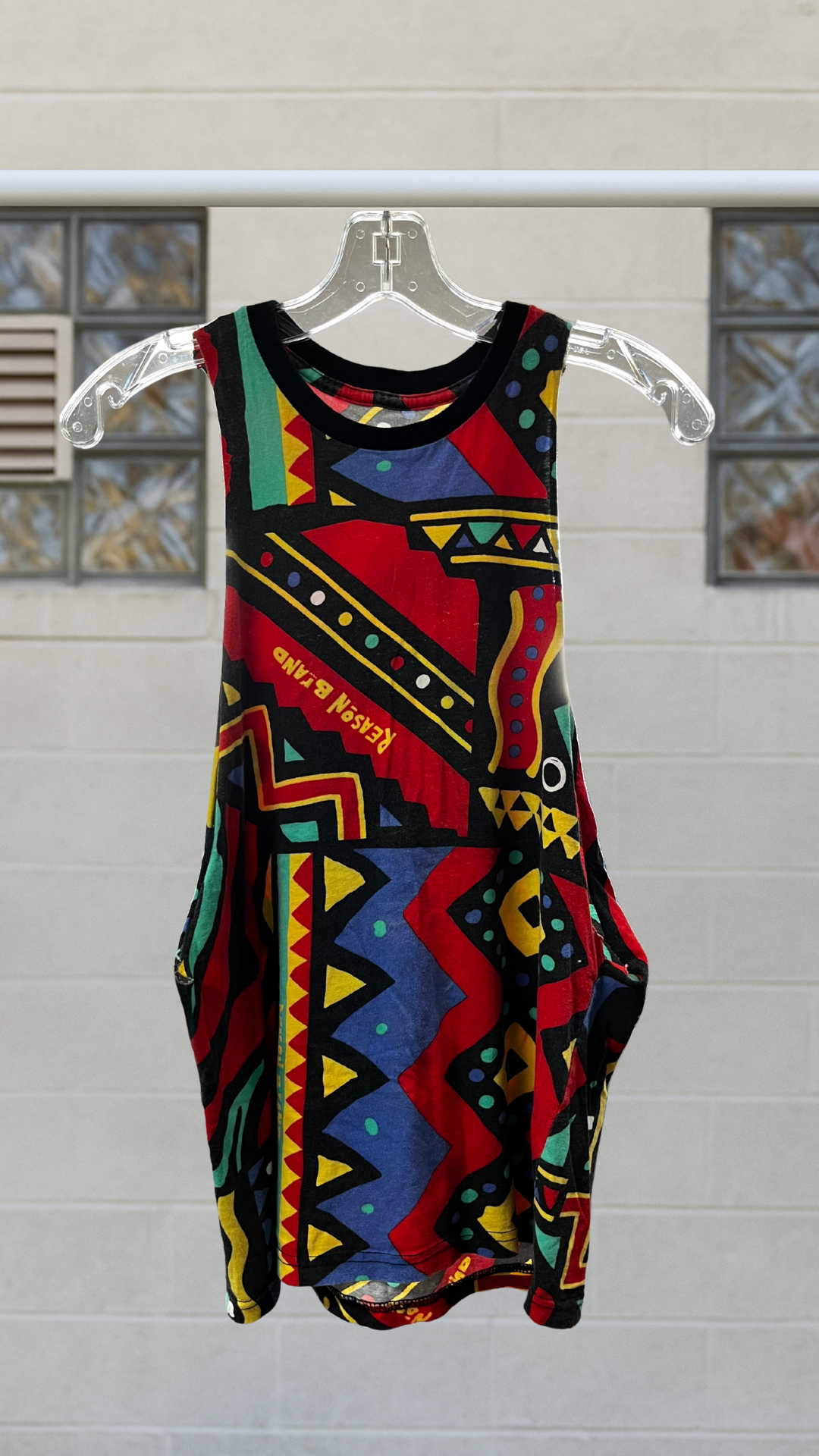 Colorful abstract sleeveless tank with drop armholes and bold geometric pattern, hanging on a clear hanger.
